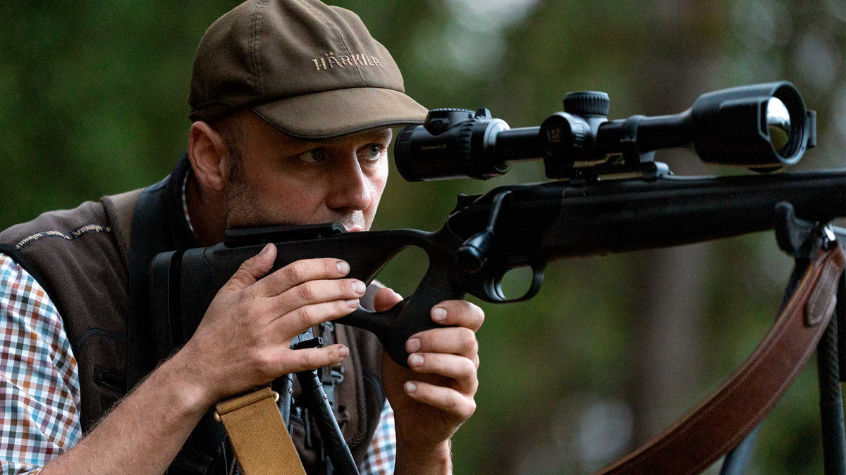 Chasseur à l’affût en forêt visant avec une carabine équipée de la lunette de tir thermique Pulsar Thermion 3